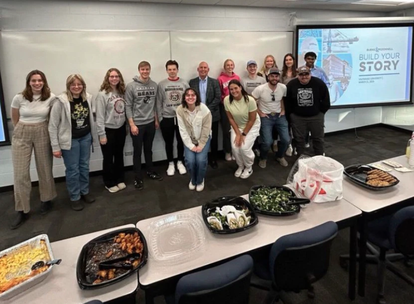 A group of people from the American Society of Civil Engineers posing in a classroom with food trays on a table in the foreground.